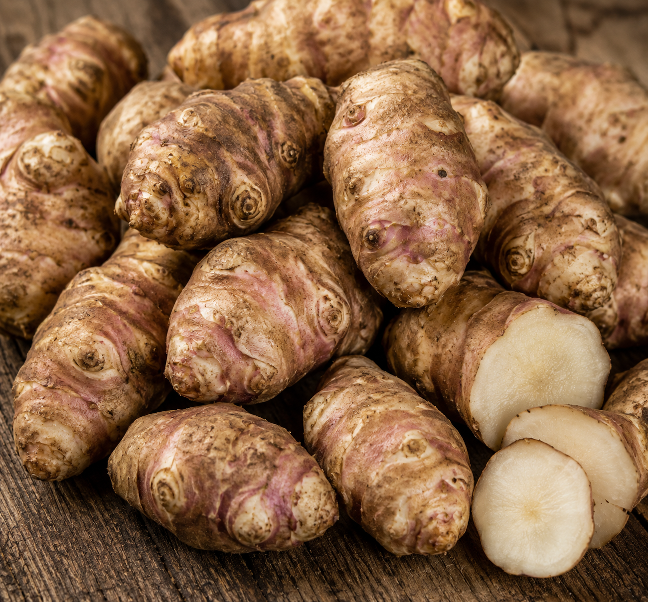 Fresh Jerusalem artichoke tubers, also known as sunchokes, with several cut pieces showing the pale interior.